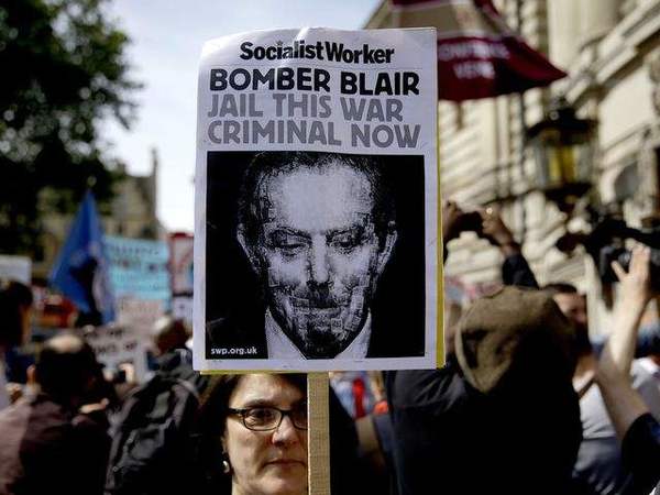 　　抗议者举着要求将布莱尔关进监狱的抗议标语牌，围聚在伦敦伊丽莎白女王会议中心外。（图片来源：新华/美联）