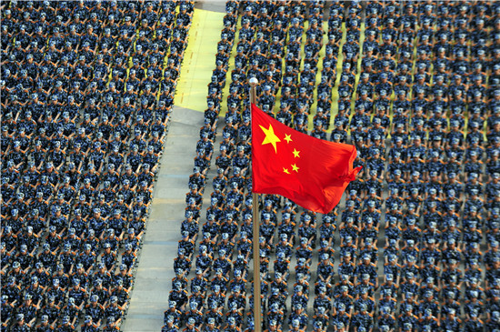 2015年9月16日，山东日照，曲阜师范大学日照校区的开学典礼举行，身着军训服装的大一新生端坐在国旗下。视觉中国供图（资料图片）