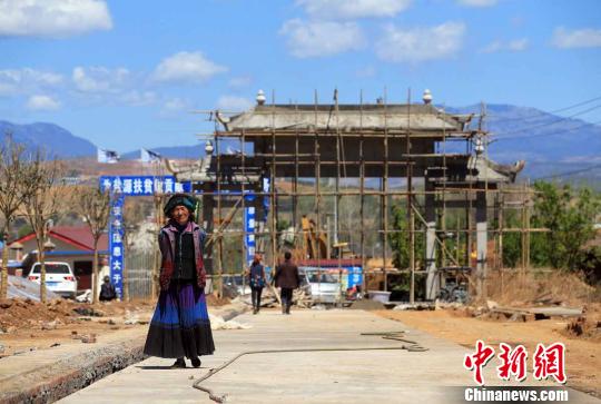 一名彝族大妈从正在修建的易地扶贫集中安置点大门进入小区　王磊　摄