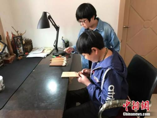 正在认真雕刻的李伟和陪伴在一旁的邢亚坤