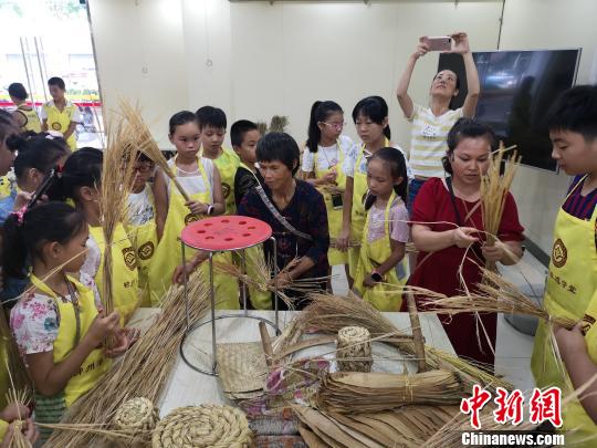8月8日，广西鹿寨县中渡草编县级传承人罗琼荣在教孩子们编制草凳。　朱柳融 摄