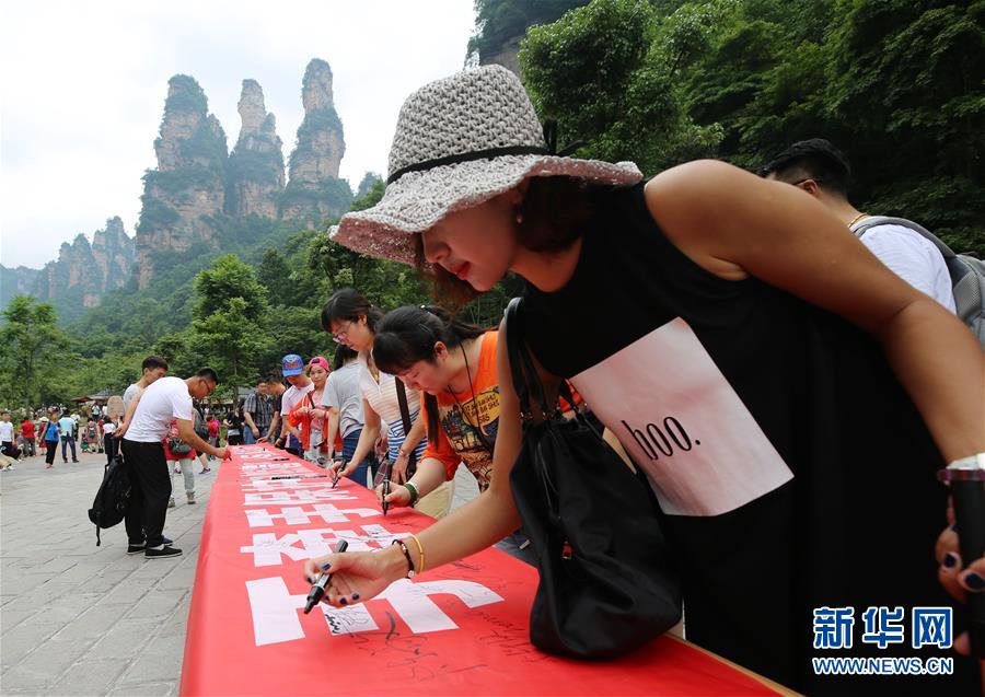 张家界武陵源,游客在"手牵手保护自然遗产,心连心共建美好家园"横幅上