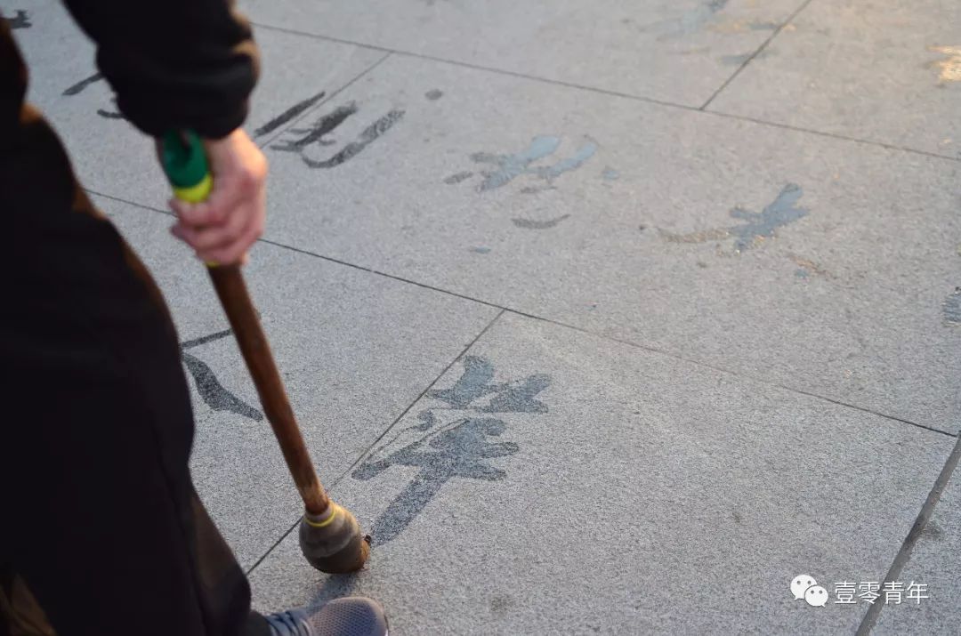 老人用地书笔在广场写字,小姑娘跃跃欲试,老人看后亲自教写书法