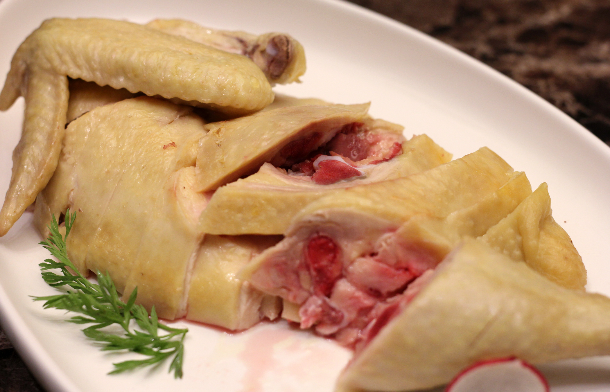 上海白切三黄鸡的做法虽然很简单:滚水里加葱,姜,酒,煮鸡至熟,冷却后